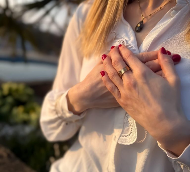 Femme en chemise blanche, mains croisées sur la poitrine, avec vernis à ongles rouge.