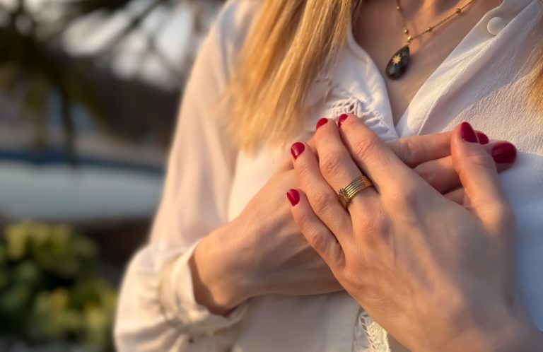 Femme avec des ongles rouges, tenant ses mains sur sa poitrine, vêtue d'une chemise blanche.