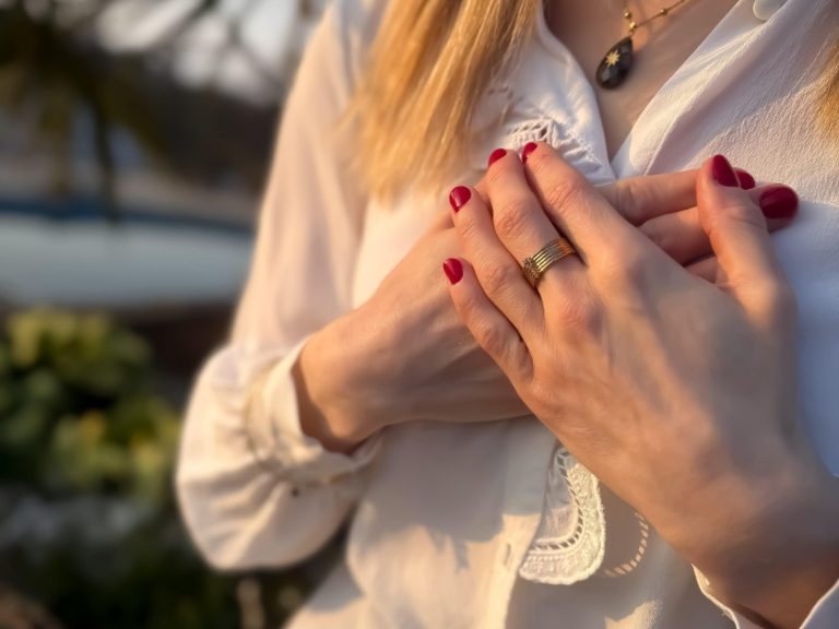 Femme en chemise blanche, mains croisées sur la poitrine, avec vernis à ongles rouge.