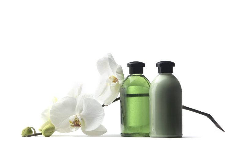 Bouteilles de produit cosmétique vertes avec une orchidée blanche à côté.