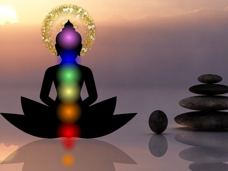 Silhouette d'une figure méditative avec chakras colorés, près de pierres empilées.